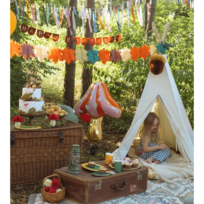 Kleurrijke herfstslinger met papieren bladeren boven een feesthoek met tipi en bosdecoratie
